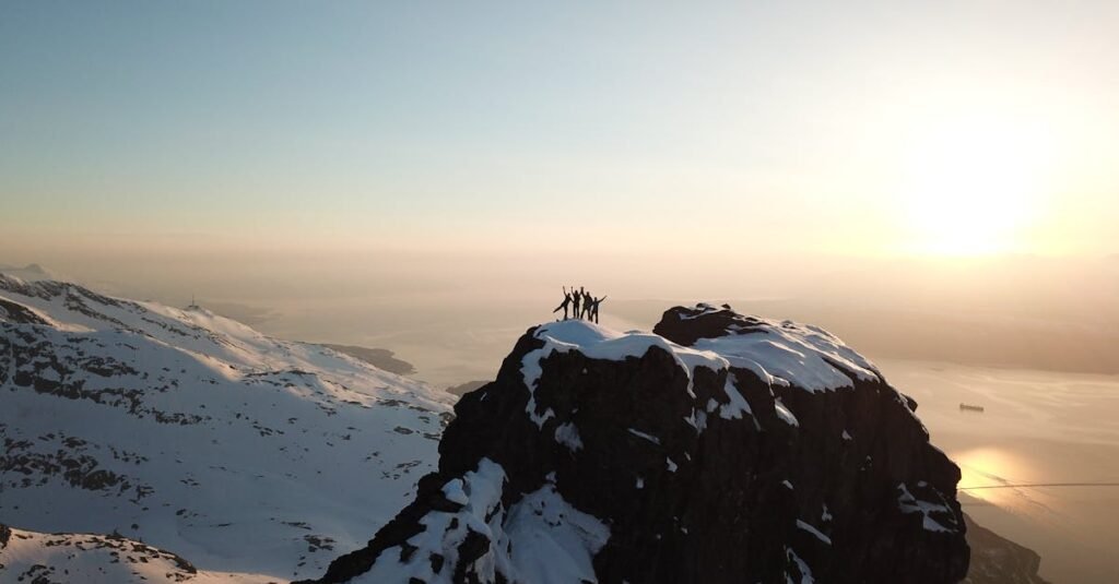 Adventurers celebrate atop a snow-covered peak in Narvik, Norway during sunrise.