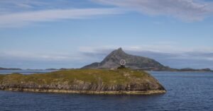 A serene coastal view featuring a grassy island and a distant mountain under a clear sky.