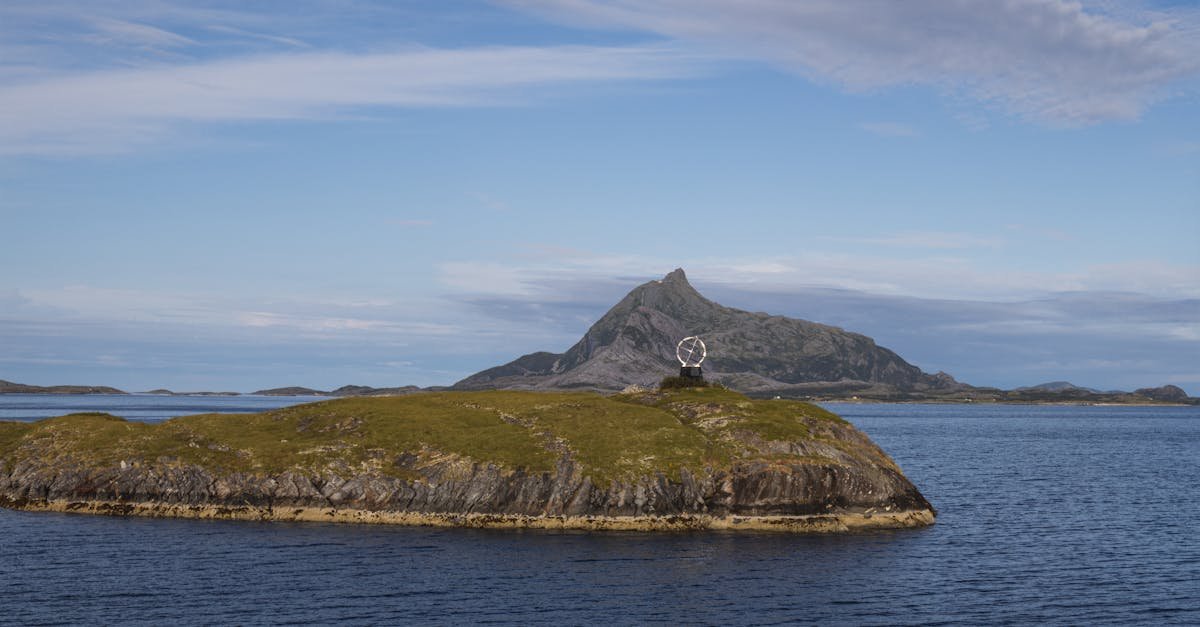 Home A serene coastal view featuring a grassy island and a distant mountain under a clear sky.