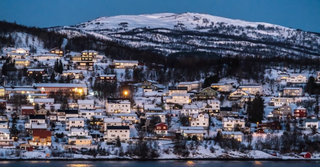 Charming snowy village set against Norwegian winter landscape illuminated at twilight.